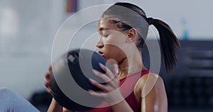 Active young woman doing Russian twists with a weighted handheld medicine ball while exercising in a gym. Fit young