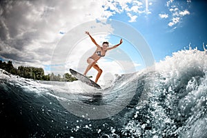 Active young woman effectively jumps on the wave on surfboard