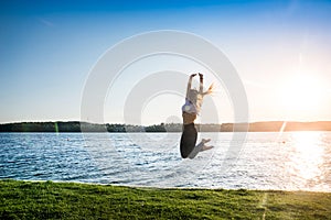 Active young woman jumping on lakeshore at sunrise