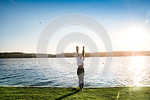 Active young woman jumping on lakeshore at sunrise