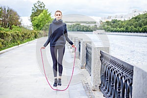 Active young woman jumping with skipping rope outdoors.