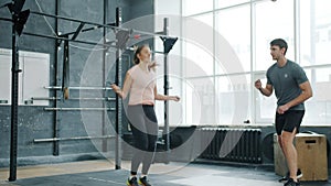 Active young woman jumping with skipping rope training with male trainer in gym