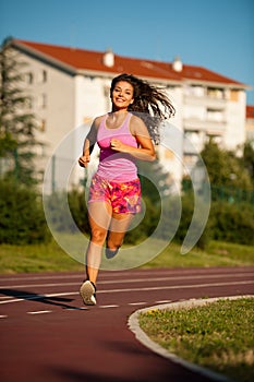 Active young woman runs on atheltic track on summer afternoon