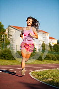Active young woman runs on atheltic track on summer afternoon
