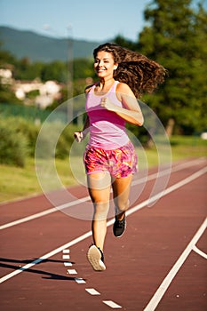 Active young woman runs on atheltic track on summer afternoon