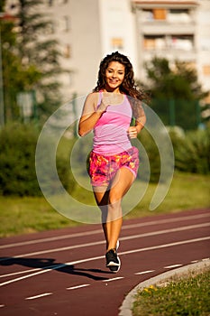 Active young woman runs on atheltic track on summer afternoon