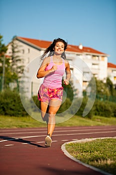 Active young woman runs on atheltic track on summer afternoon