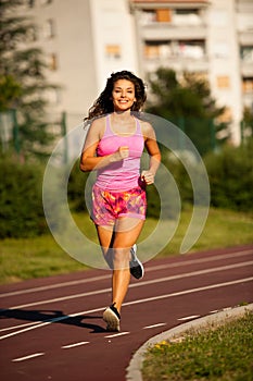 Active young woman runs on atheltic track on summer afternoon