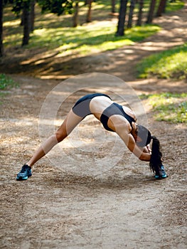 Active young woman workout outside, doing stretching exercises on legs and hands on the left side,  on park background