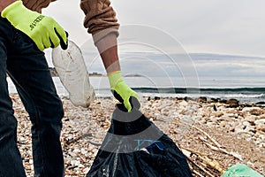 An activist puts a plastic bottle in a garbage bag. The concept of environmental conservation and coastal zone cleaning.