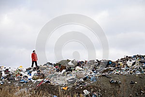 Activist standing on landfill, on large pile of waste with dark clouds above. Environmental concept and eco activism.