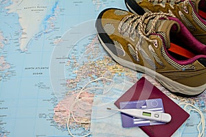 Walking boots on world map and face mask passport thermometer insurance card . Stop spreading coronavirus