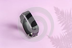 Activity smart tracker on light pink background. Black fitness health watch with fern shadow, sport bracelet