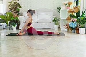 Activity women sitting on mat in front of white sofa while doing position yoga Anjaneyasana in living room. Relaxation girl