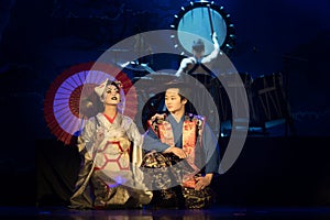 Actor and actress in traditional kimono and fox mark sitting in the dark stage with umbrella and