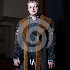 Actor dressed historical costume in interior of old theater.