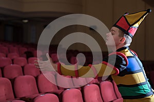 Actor dressed jester`s costume in interior of old theater.