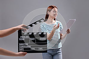 Actress performing role while second assistant camera holding clapperboard on grey background, selective focus