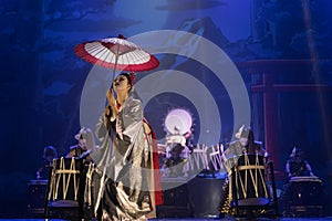 Actress in traditional kimono on the dark stage with umbrella and taiko drummers