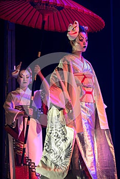 Actress in traditional kimono and fox mark gradually goes and her assistant holds umbrella above