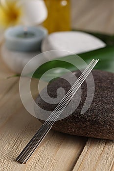 Acupuncture needles and spa stone on wooden table