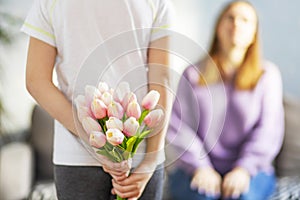 Acute son giving his mother a bouquet of tulips congratulating her on mother& x27;s day while celebrating the holiday at home