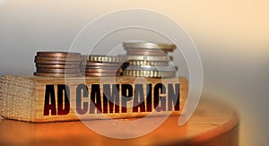 Ad campaign words on wooden block and coins stacks. Advertising marketing promotion business concept