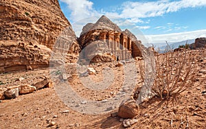 Ad Deir - Monastery - ruins carved in rocky wall at Petra Jordan, mountainous terrain with blue sky background, small dry bush