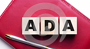 ADA Americans with Disabilities Act is made up of wooden cubes that stand on a burgundy notebook near the pen. Business concept