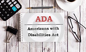 ADA Americans with Disabilities Act is written in a white notepad near a calculator, coffee, glasses and a pen. Business concept