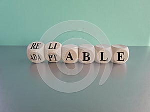 Adaptable or reliable symbol. Turned wooden cubes and changed the word adaptable to reliable. Beautiful blue background, grey