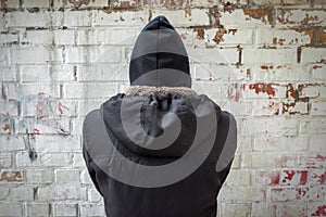 Addict in black on a brick wall background. The view from the back. Man experiencing a drug addiction crisis. Addiction concept