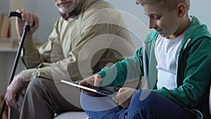 Addicted boy playing tablet game and sad grandfather looking him, condemnation