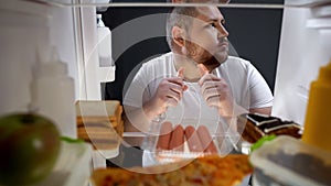 Addicted man secretly eating sausages at night near fridge, unhealthy nutrition photo