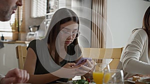 Addicted teenage girl using mobile phone during breakfast at the table.
