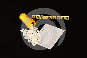 Addiction spelled out with tiles, spilled prescription pills on a prescription pad on a black background