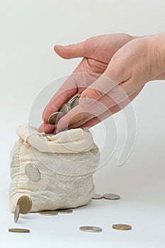 Adding coins to a small bag of money. Hands close-up. Falling coins. Vertical photo, white background. Concept - enrichment