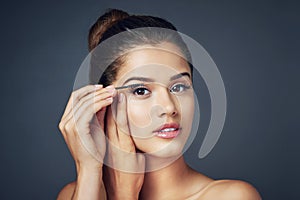 Adding that extra oomph with mascara. Studio shot of a beautiful young woman applying mascara while posing against a