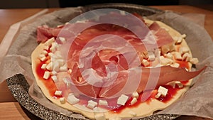 Adding liberal amounts of ham on a pizza dough.