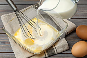 Adding milk to whisked eggs at wooden table photo