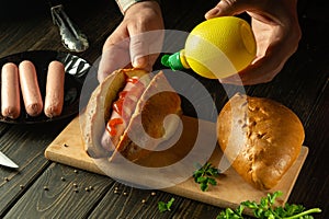 Adding mustard by the cook's hands to a hot dog for flavor. The concept of cooking fast food or street food. Copy space