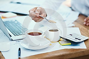 Adding some sweetener to his drink. an unrecognizable businessman pouring a teaspoon of sugar into a cup of tea in an