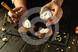Adding sour cream for an exquisite taste to fried cutlets by the hands of the chef. The process of serving a delicious meat dish