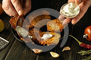 Adding sour cream for an exquisite taste to potato pancakes with the hands of a chef. The process of serving a delicious vegetable