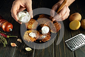 Adding sour cream to pancakes with a spoon in the hands of a man. Low key concept for preparing a vegetarian dinner