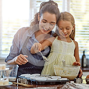 Adding a spoonful of love. a mother and her daughter baking in the kitchen.