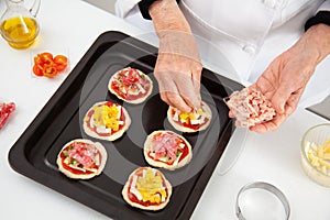 Adding toppings to the mini pizzas. Adding ham to the Hawaiian pizza. Delicious homemade mini pizzas preparation