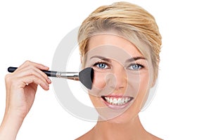 Adding a touch of color. A young woman applying blush to her cheeks while isolated on white.