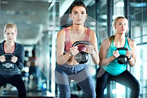 Adding weights can really change your game. three attractive young women working out with kettle bells in the gym.