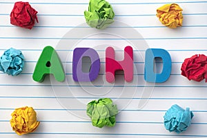 ADHD. The abbreviation ADHD on a notebook sheet with some colorful crumpled paper balls around it. Close up.